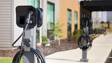 Estação de carregamento para veículos elétricos com cabo conectado, em frente a fachada moderna de um edifício com janelas amplas e área pavimentada.