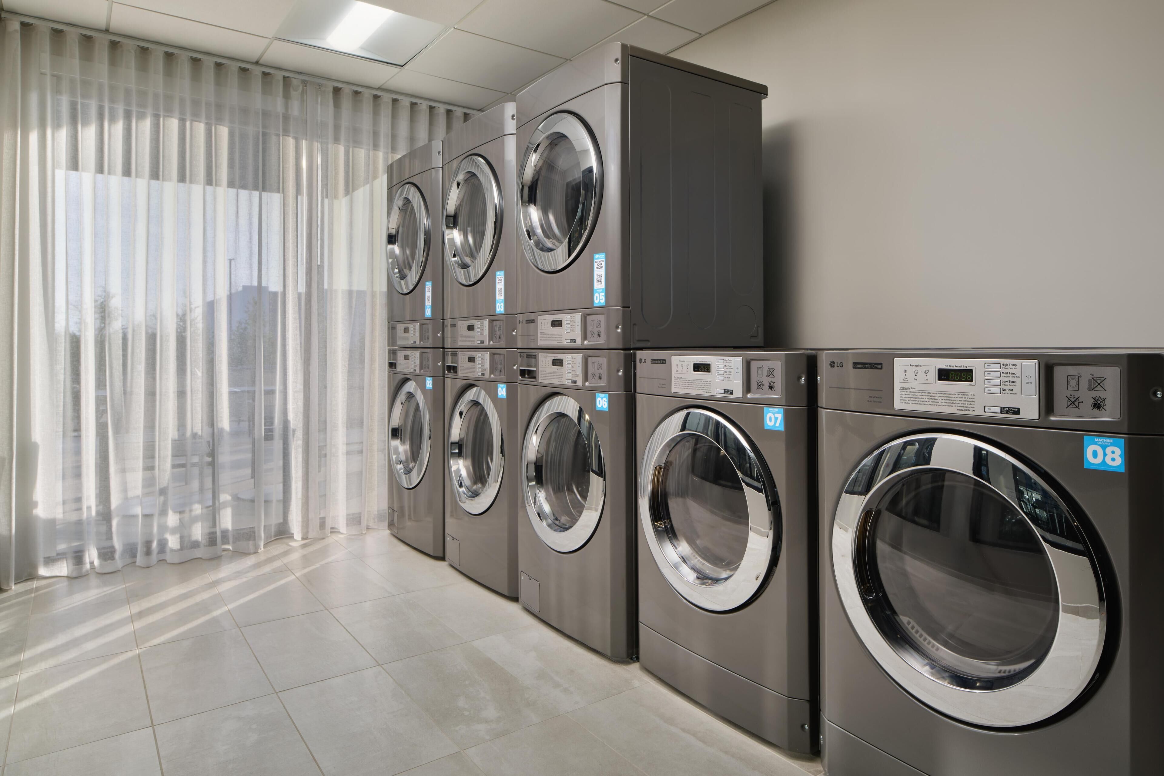 A row of modern, stainless steel front-loading washers in a commercial setting.