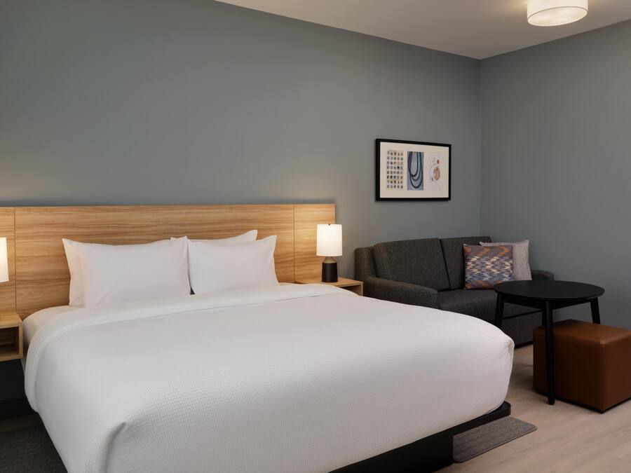 Een hotelkamer met een groot bed, een grijze bank, een klein tafeltje en een bruin poef.