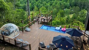 Une terrasse en bois avec une piscine, des chaises longues et des parasols.