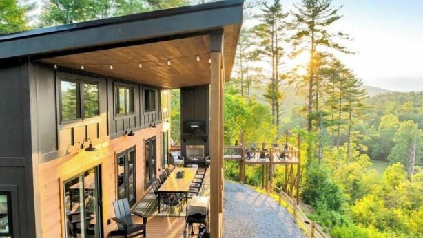 Une cabane moderne dotée d’une terrasse, de grandes fenêtres et d’une cheminée.