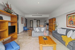 A modern living room with a grey sofa, blue armchair, wooden coffee table, and a TV on a wooden stand.