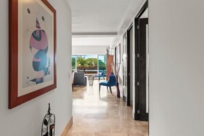 A hallway with a framed abstract painting, a metal sculpture, and a view of a balcony with outdoor seating.