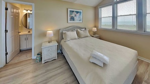 Een slaapkamer met een bed, nachtkastjes, een raam met jaloezieën, een deur naar een badkamer en een schilderij aan de muur.