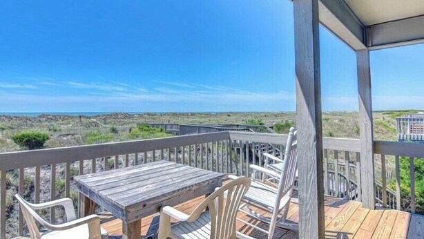 Een houten terras met een tafel en stoelen, met uitzicht op een strand en duinen.
