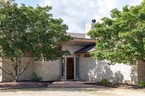 A house with a stone facade, a wooden door, and a brick chimney. - Round Top Designer Home (Round Top)