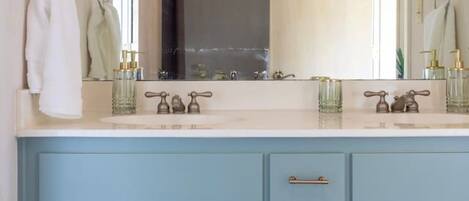A bathroom with a large mirror, two sinks, and a blue vanity with drawers.