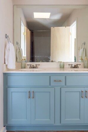 Une salle de bain dotée d’un grand miroir, de deux lavabos et d’un meuble-lavabo bleu avec des tiroirs.