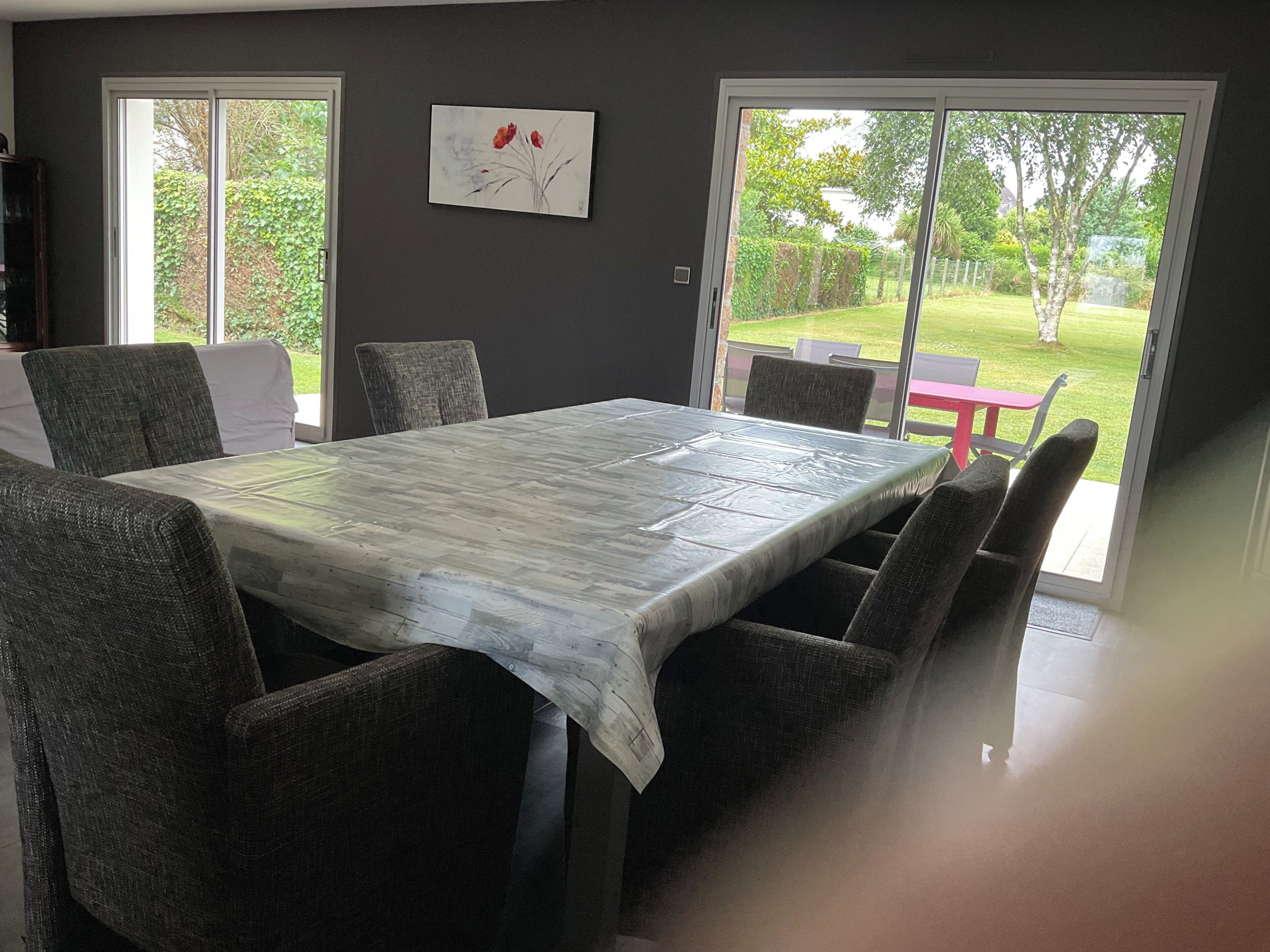 A dining area with a large table, four chairs, and a view of a garden through glass doors.