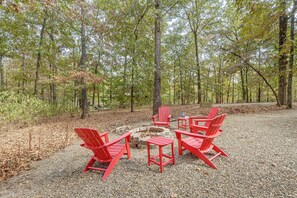 Un entorno boscoso con una hoguera, sillas Adirondack rojas y una mesa.