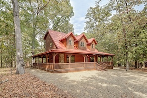 A wooden cabin with a porch and a stone wall, surrounded by trees. - Near Choctaw Landing | 2 King Bedrooms | Game Loft (Broken Bow)