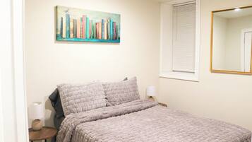 Un dormitorio con una cama, un cuadro de libros, una ventana con persianas y un espejo.