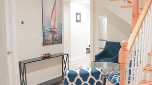 Una sala de estar moderna con una mesa de centro de vidrio, un sillón estampado en azul y blanco, y un cuadro de un velero en la pared.