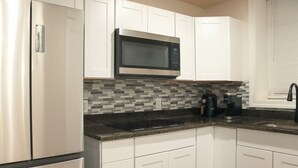 Una cocina moderna con gabinetes blancos, un refrigerador de acero inoxidable, un microondas negro y un salpicadero de azulejos.