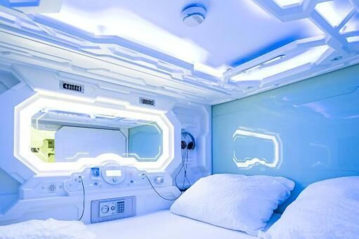 A futuristic room with a bed, control panels, and a neon-lit wall.