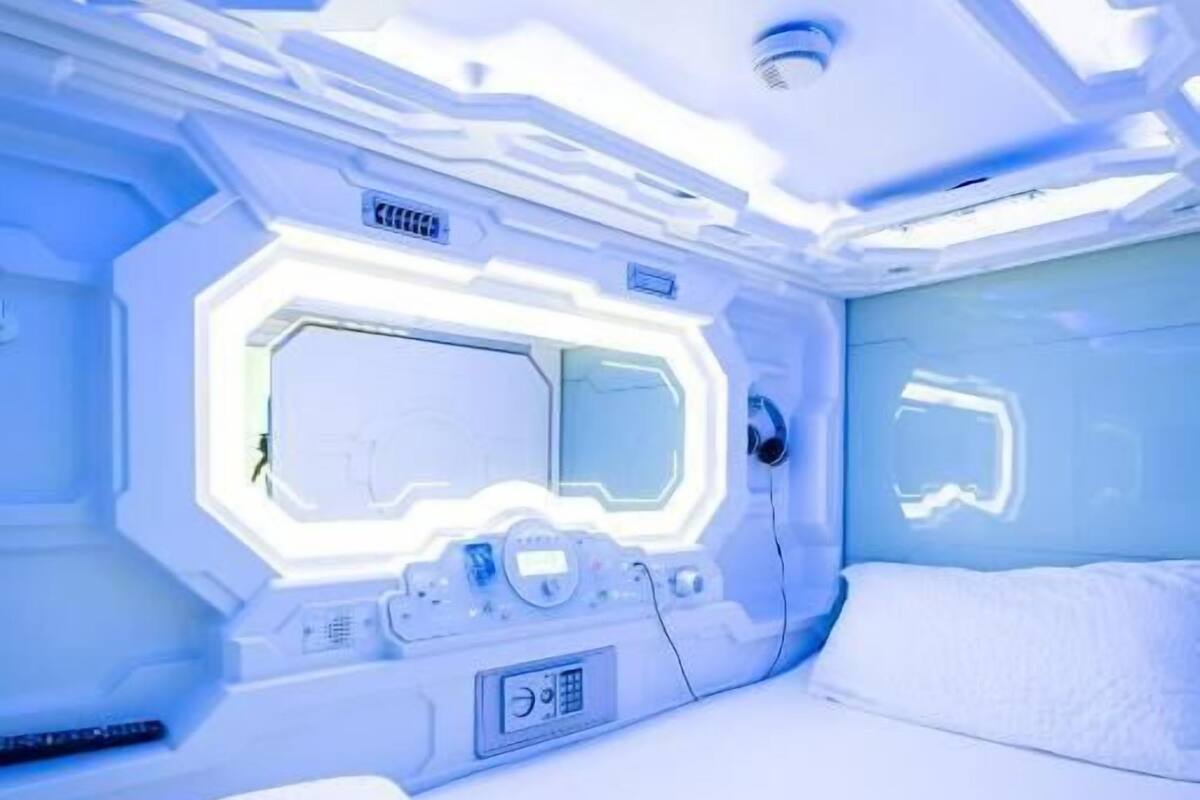 A futuristic room with a bed, a control panel, and a large window.