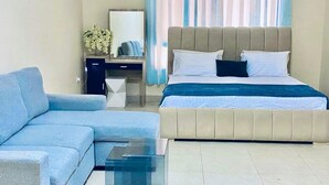Una habitación de hotel moderna con un sofá, una cama, un escritorio y una mesa de centro de vidrio.
