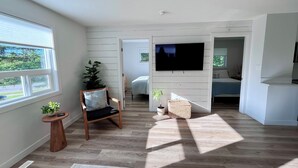 A modern living room with a flat-screen TV, wooden flooring, and a large window. - Alpine Escape-Completely Renovated Home, 20 minutes from Jasper Park Gates (Hinton)