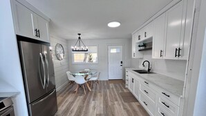 A modern kitchen with white cabinets, a stainless steel refrigerator, a dining table with chairs, and a pendant light. - Alpine Escape-Completely Renovated Home, 20 minutes from Jasper Park Gates (Hinton)