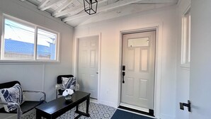 A hallway with a white door, a bench with a vase of flowers, patterned floor tiles, and a ceiling with exposed beams. - Alpine Escape-Completely Renovated Home, 20 minutes from Jasper Park Gates (Hinton)
