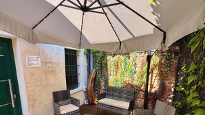 Área de varanda coberta com móveis de vime, mesa de vidro e parede de tijolos com plantas trepadeiras.