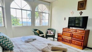 A bedroom with a bed, a dresser, a television, and large windows.
