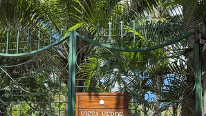 A wooden sign with the text "VISTA VERDE BEACH HOUSE" on a metal fence.