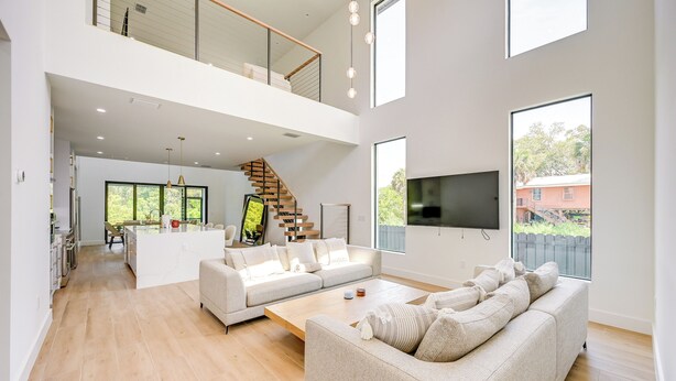 A spacious living area with a high ceiling, a staircase leading to an upper level, a large flat-screen TV mounted on the wall, and a view of the outdoors through large windows. - 3 Mi to Naples Beach: Luxurious Home w/ Pool! (Naples)
