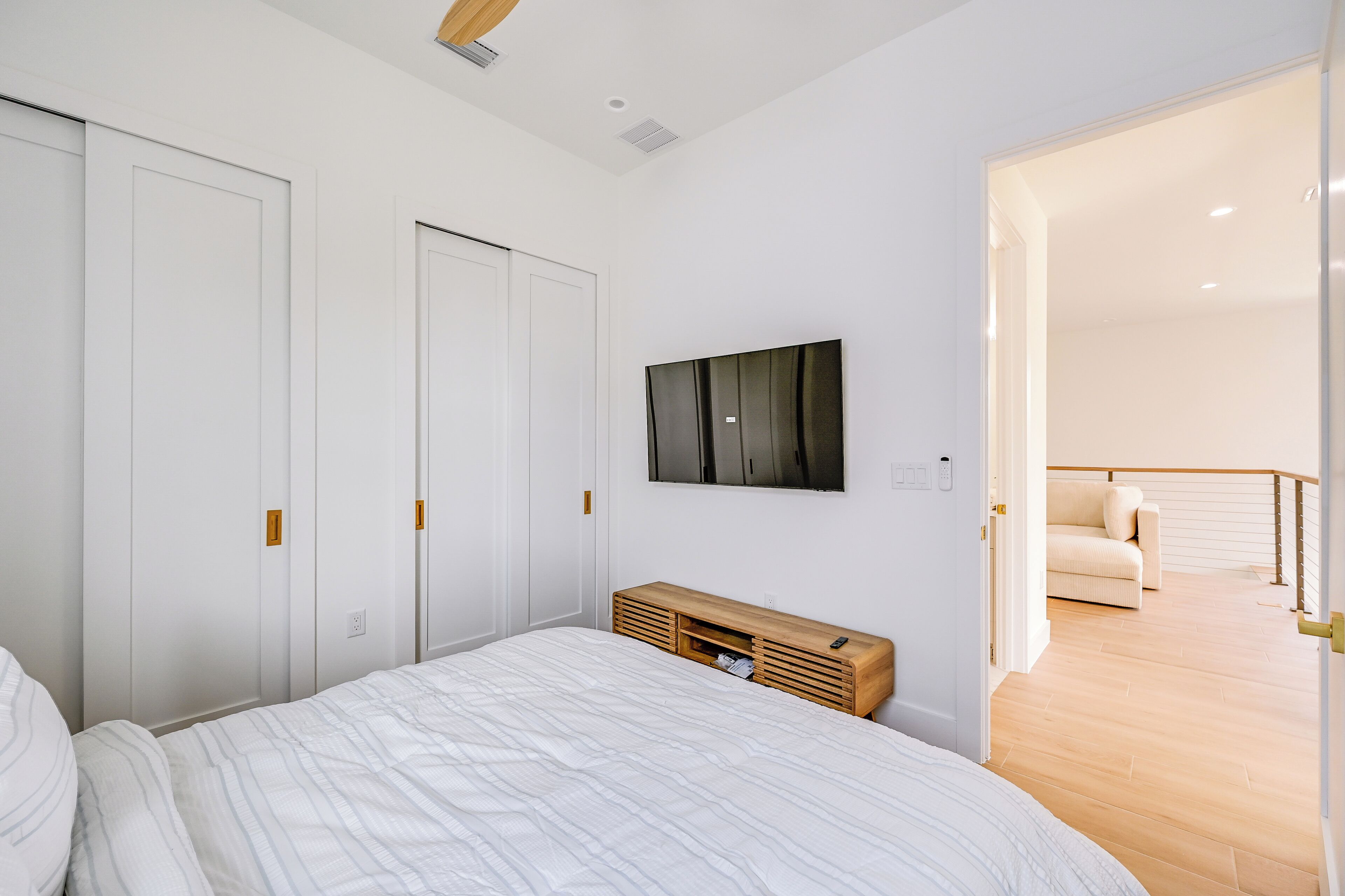 Una camera da letto con un letto, un comodino in legno, una TV fissata al muro e una porta che dà su un balcone.