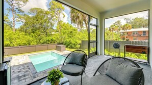 A modern outdoor living area with a pool, comfortable seating, and a view of a lush garden and neighboring buildings. - 3 Mi to Naples Beach: Luxurious Home w/ Pool! (Naples)
