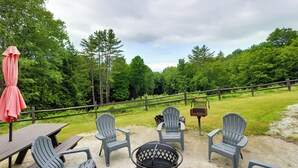 Uma área de piquenique com cadeiras Adirondack, uma lareira e uma mesa de madeira.