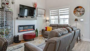 Una sala de estar con chimenea, un televisor de pantalla plana grande, un sofá y un otomano rojo.