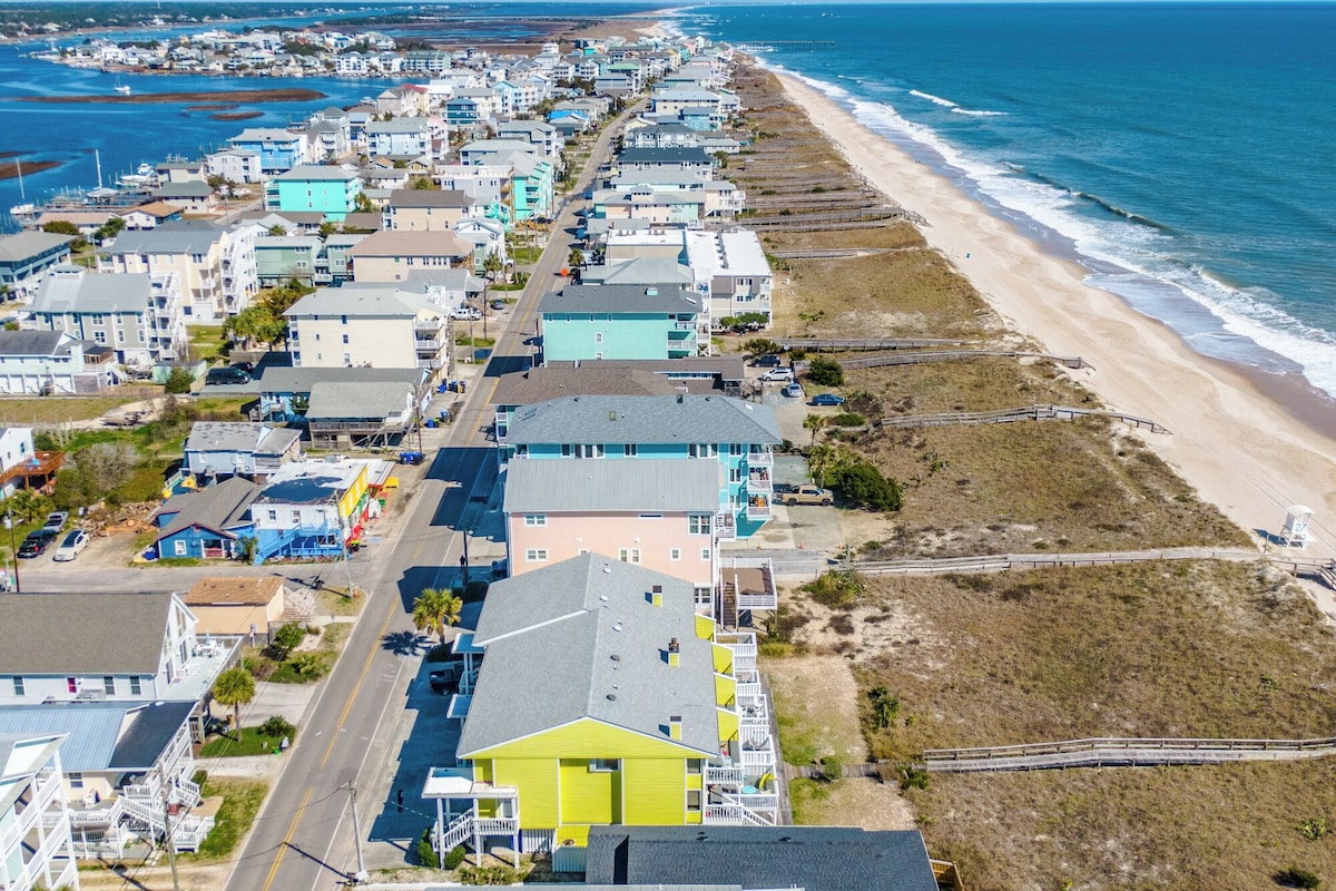 A coastal residential area with houses along the beach, a clear view of the ocean, and a road running parallel to the shore.