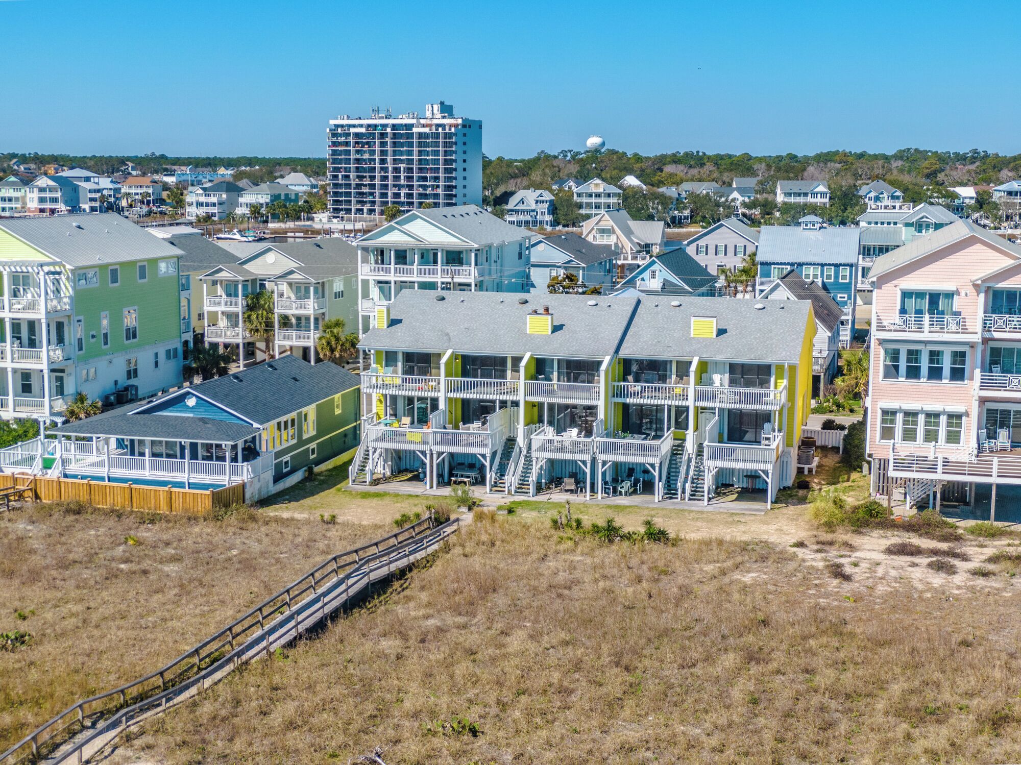 A coastal residential area with multi-story houses featuring balconies and a wooden boardwalk.