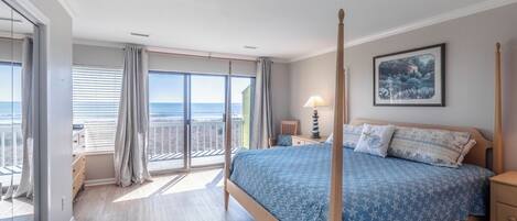 Una camera da letto con un letto a baldacchino, un balcone con vista sulla spiaggia e un quadro appeso al muro.