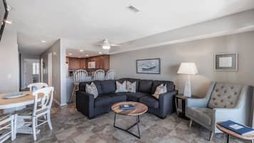 A living room with a dark grey sofa, a round coffee table, and a dining area with white chairs.