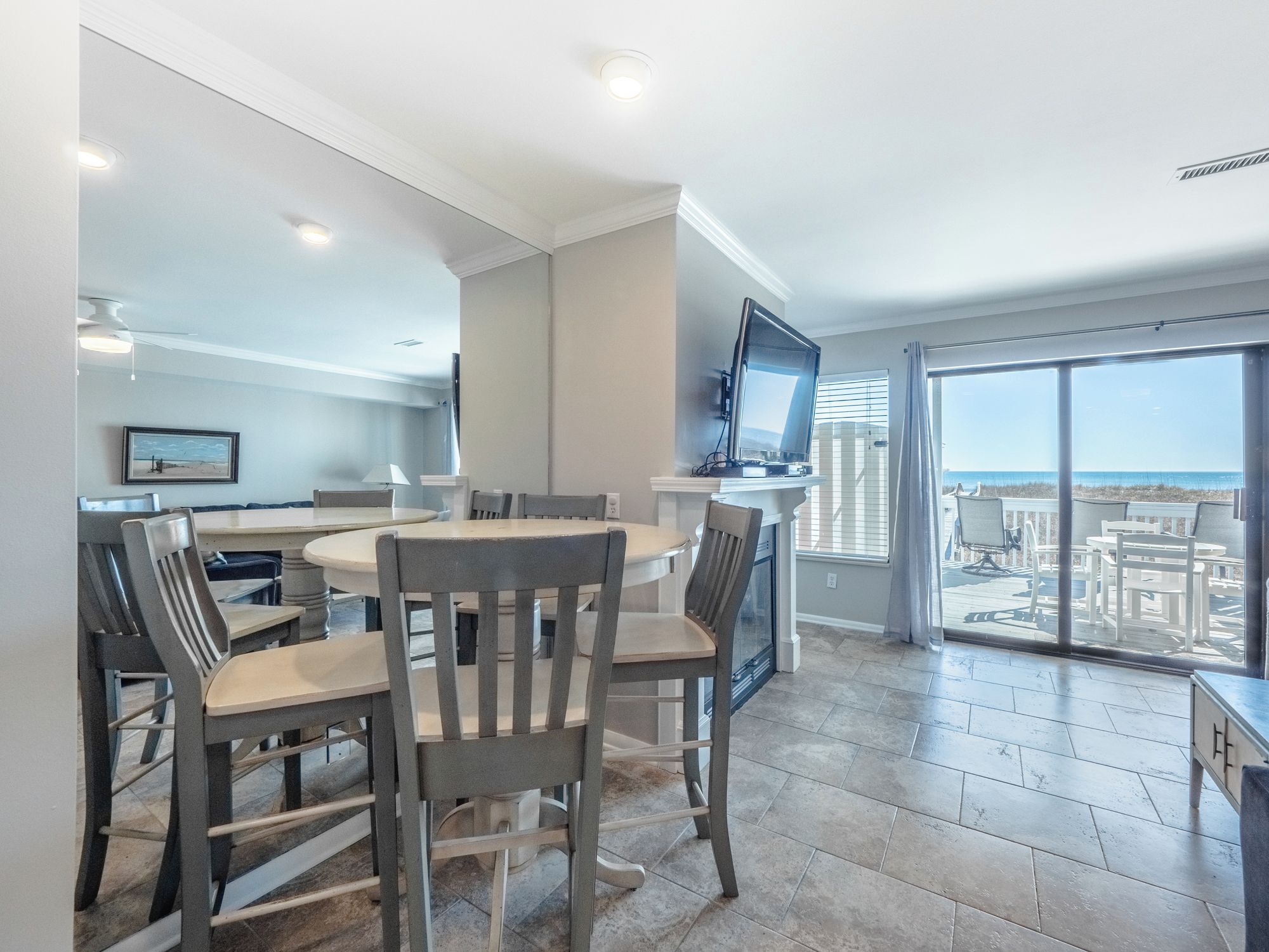 A modern kitchen with a dining area, a TV, and a view of the beach.