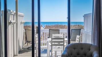 A deck with a view of the beach, white furniture, and a grey armchair.
