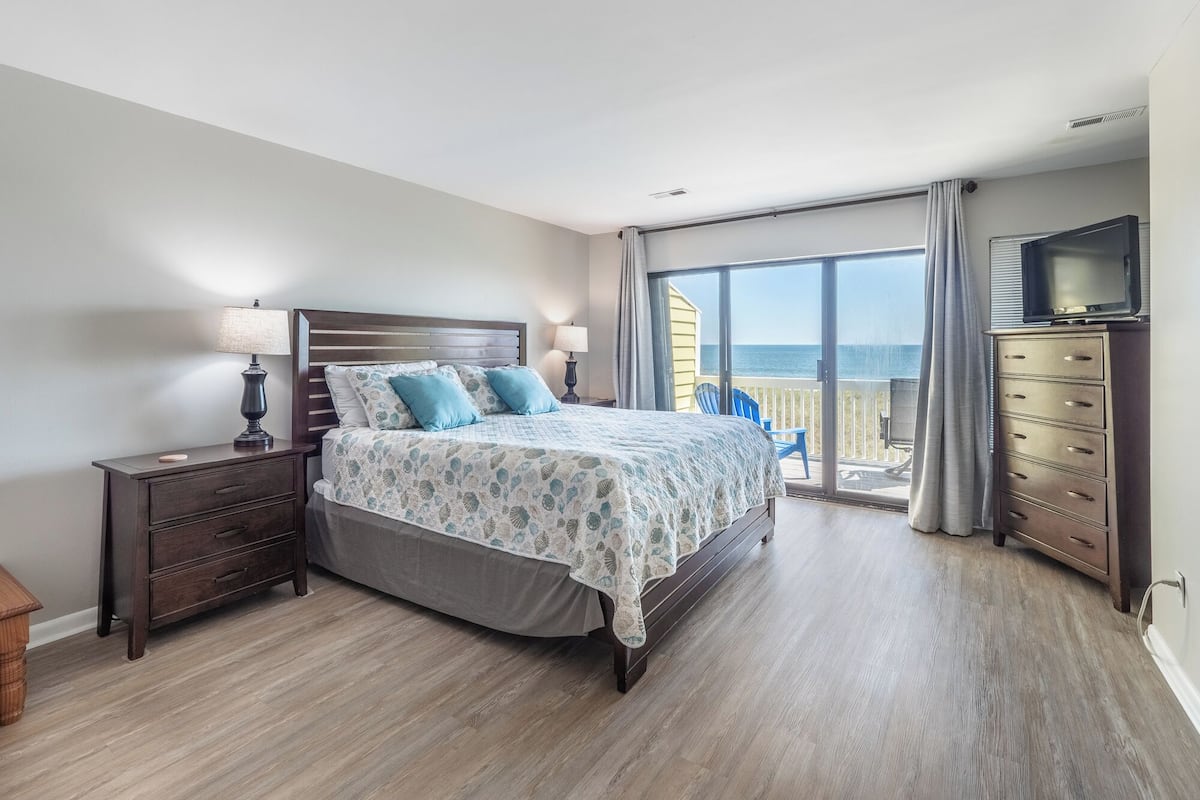 Un dormitorio con una cama grande, un aparador, un televisor y un balcón con vista al mar.