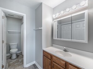A bathroom with a toilet, vanity, and mirror. - Here Comes The Sun by Carolina Retreats (Carolina Beach)