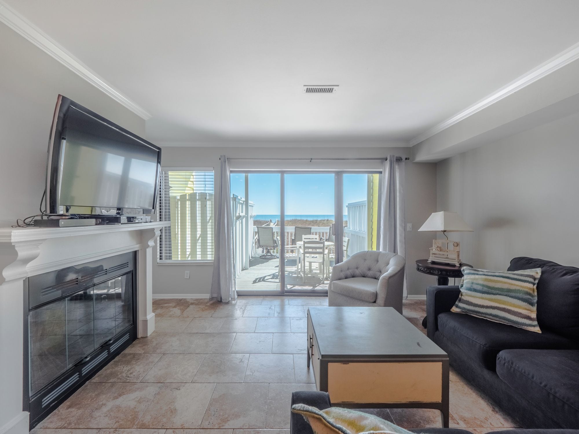 Un salón moderno con chimenea, un televisor de pantalla plana, un sofá, una mesa de centro y un balcón con vistas a la playa.
