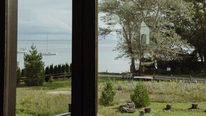 A view from a window overlooking a grassy area with trees, a small tower-like structure, and boats on the water.