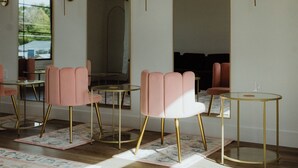 A modern interior with pink chairs, round tables, and arched doorways.