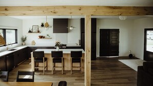A modern kitchen with wooden beams, a dining area with chairs, and a view of the outdoors.