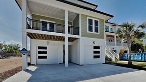 Een tweelaags huis met een balkon op de bovenverdieping, een garage met drie deuren, en een zwembad op de achtergrond.