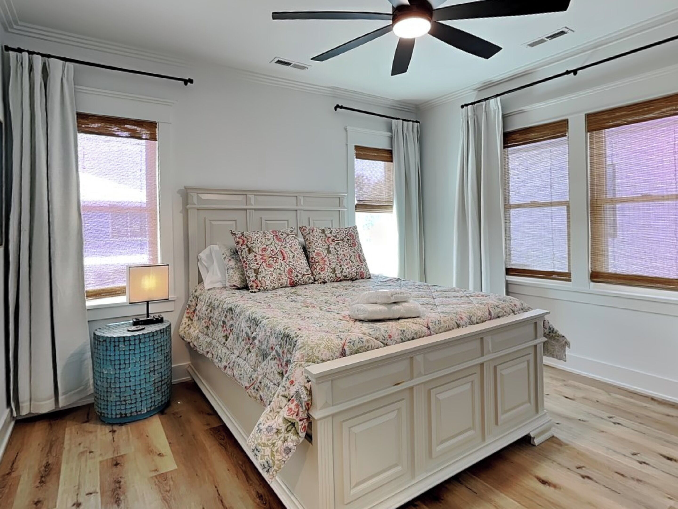 A bedroom with a bed, a ceiling fan, a bedside lamp, and a round blue side table.