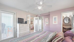 A bedroom with a bed, dresser, ceiling fan, and a bathroom with a sink and mirror. - A Place At The Beach #1a- Badabing by Carolina Retreats (Carolina Beach)