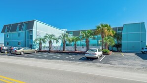 A multi-story hotel with a blue exterior, parking lot, and palm trees. - A Place At The Beach #1a- Badabing by Carolina Retreats (Carolina Beach)
