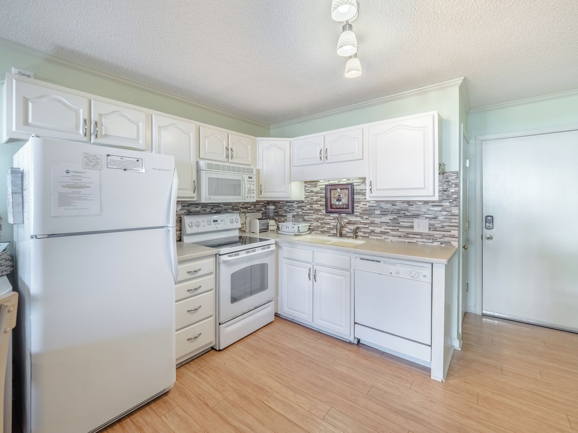 A kitchen with white cabinets, a refrigerator, a microwave, an oven, a sink, and a dishwasher.