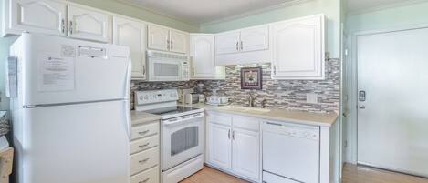 A kitchen with white cabinets, a refrigerator, a microwave, an oven, a sink, and a dishwasher.
